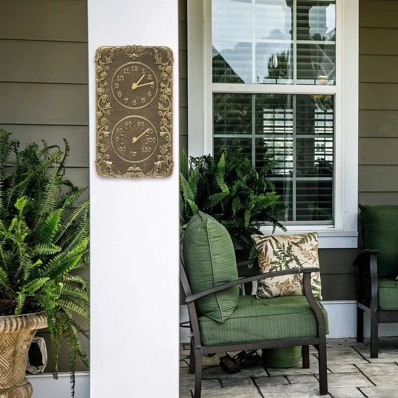 Whitehall Acanthus clock and thermometer displayed on a pillar with green outdoor furniture and ferns